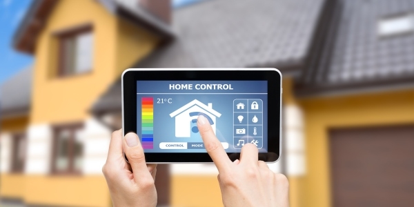 Das Bild zeigt ein Haus im Hintergrund und ein Tablet mit Hausautomationssystem im Vordergrund. 