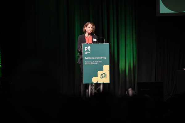 Das Bild zeigt die Vorstandsvorsitzende des Forschungszentrums Jülich, Prof. Dr. Astrid Lambrecht, hinter einem Podium mit Mikrofonen und der Aufschrift „Jubiläumsveranstaltung“. 